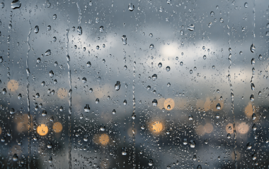 Illustrative raindrops on a window beneath a grey sky