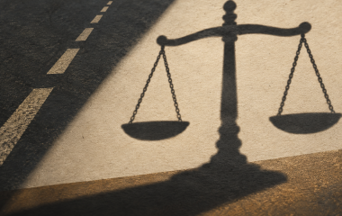 Illustrated shadow of scales of justice beside a road-line motif