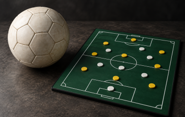 Conceptual illustration of a football beside a tactics board with yellow and white counters on a tabletop.